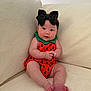 baby, infant, watermelon_romper, black_bow, headband, couch, sofa, living_room, sitting, chubby_cheeks, barefoot, toes, cute, portrait, pink_cheeks, blue_eyes, plush_fabric, home_interior, soft_lighting, adorable
