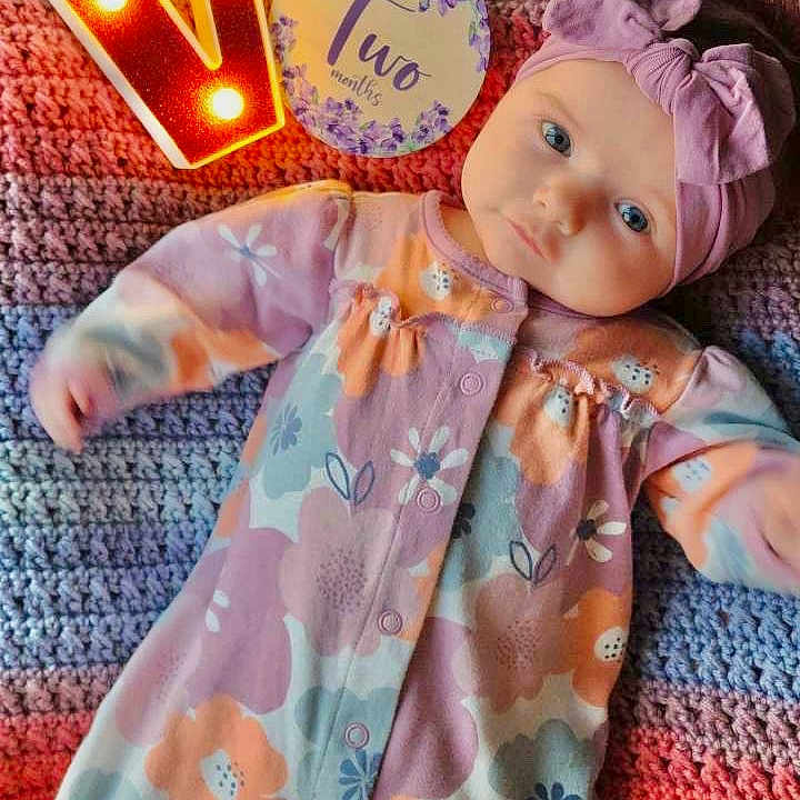 Violet is registered to the contest to win money with this photo: baby, bonnet, cap, clothing, doll, face, hat, head, number, pajamas, person, sleeve, symbol, text, toy