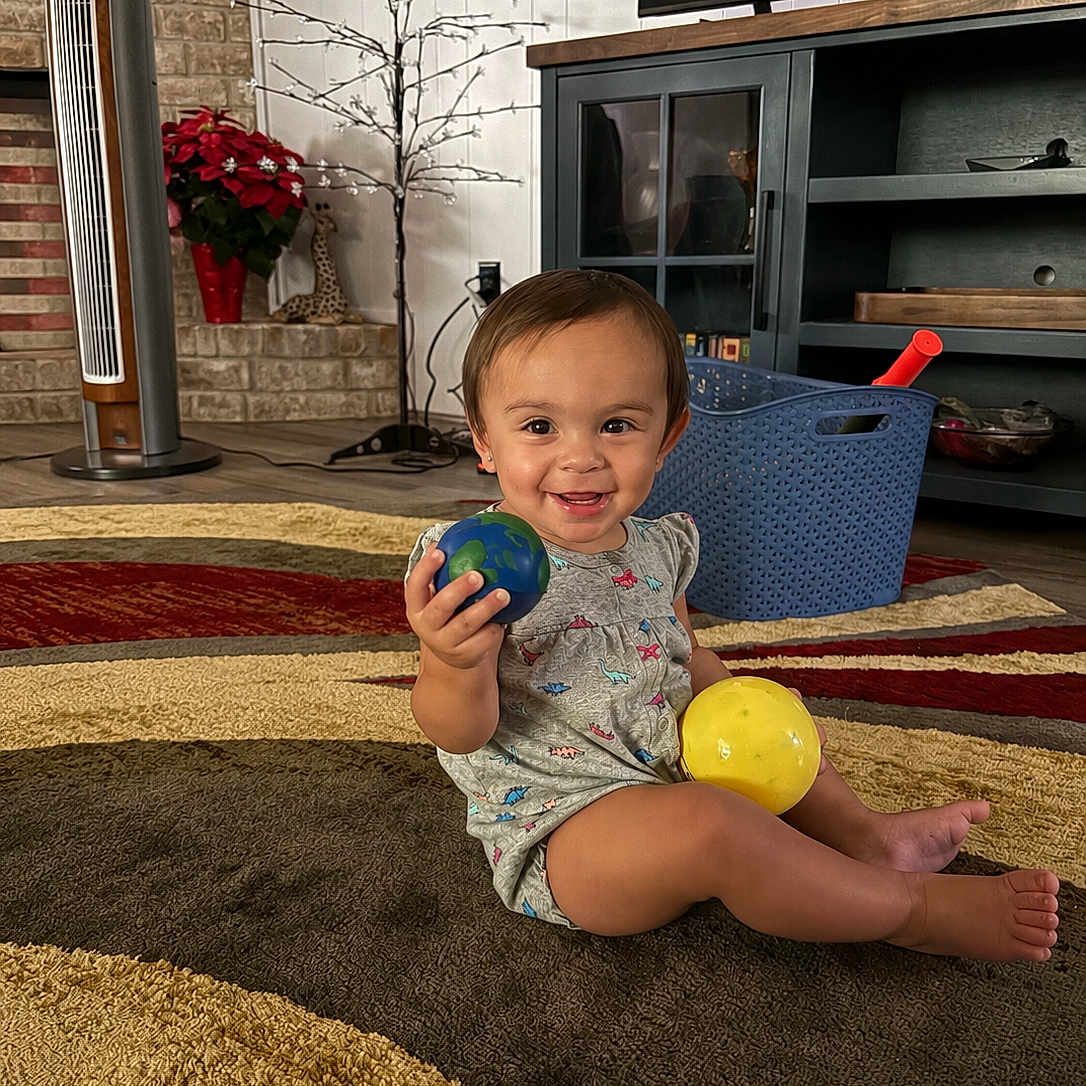Azalea joined the competition — help win amazing prizes! toddler, child, smiling, indoor, rug, toy, ball, basket, living_room, fan, plant, furniture, floor, clothing, cute, happy, person, play, home, decor