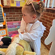 Evelyn is registered to the contest to win money with this photo: toddler, child, girl, plush_toy, rocking_horse, indoor, playroom, toy, brick_wall, white_clothing, necklace, pink_sunglasses, hairstyle, focused, furniture, carpet, colorful, window, person, cute