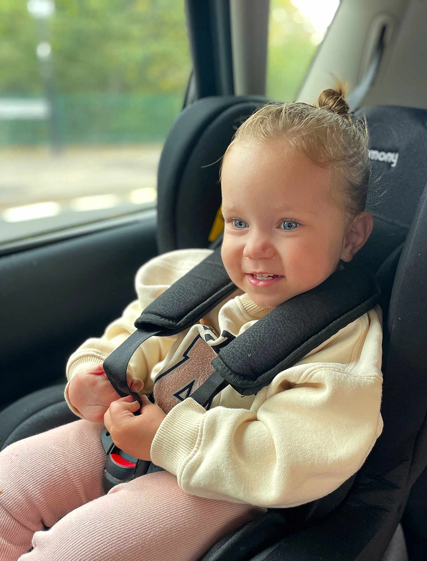 Evelyn is registered to the contest to win money with this photo: child, toddler, car_seat, safety_harness, blue_eyes, smiling, sweater, pink_pants, hair_bun, window, car_interior, seatbelt, happy, cute, indoor, portrait, baby, seat, daylight, closeup