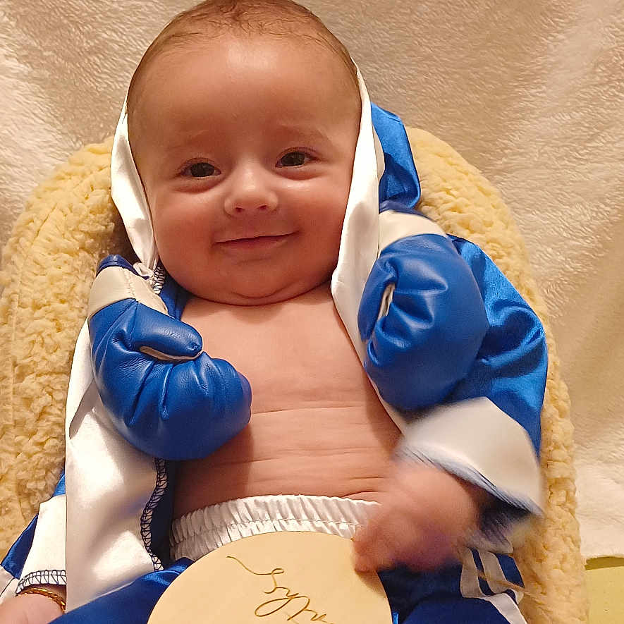 Taydann participe au concours pour gagner de l'argent avec cette photo : baby, blue_shorts, boxing_gloves, child, chubby, costume, cute, happy, indoors, infant, plush_blanket, portrait, relaxed, sitting, skin, small_hands, smiling, soft_texture, wooden_plaque, young