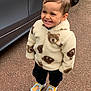 toddler, child, smiling, jacket, teddy_bear_pattern, footwear, slippers, cartoon_character, outdoor, pavement, car, vehicle, standing, happy, cute, portrait, clothing, warm_clothes, young_child, person