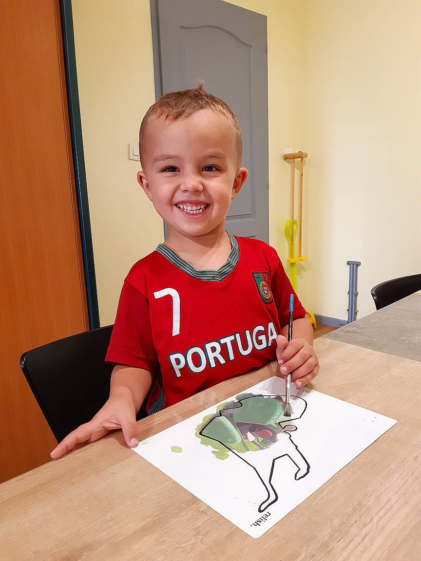 Anthonio a rejoint le concours — aidez-le/la à gagner de superbes lots ! chair, child, desk, flooring, fun, happy, hardwood, jersey, joy, person, play, room, sitting, sleeve, smile, t_shirt, table, toddler, top, varnish