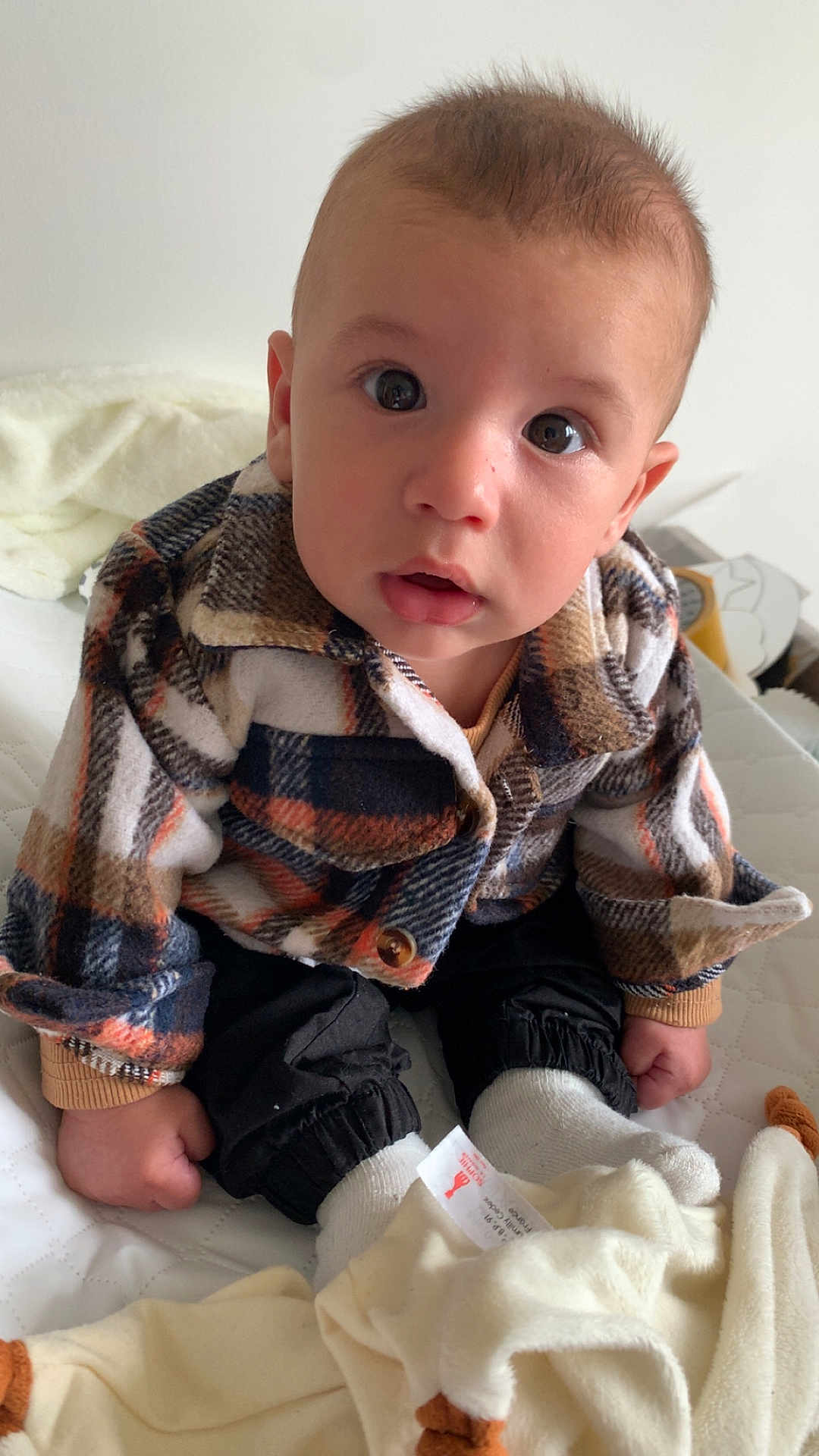 Maylan a rejoint le concours — aidez-le/la à gagner de superbes lots ! baby, bed, blanket, child, clothing, cozy, curious, cute, expression, face, feet, hands, indoors, infant, plaid_jacket, portrait, sitting, soft_toy, warm, white_socks
