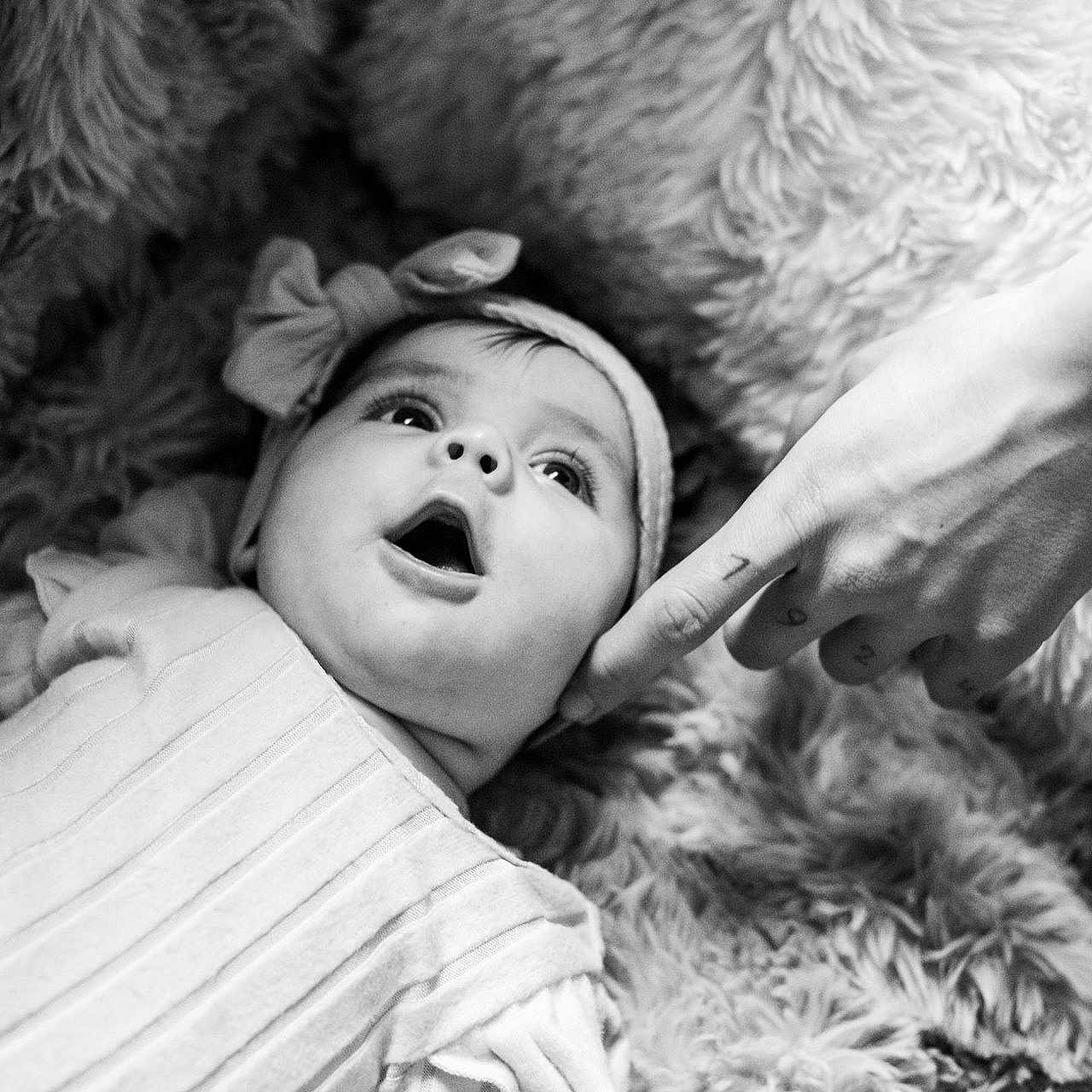 Aminaya participe au concours pour gagner de l'argent avec cette photo : baby, black_and_white, child, closeup, clothing, cozy, curious, cute, expression, face, finger, hand, headband, indoors, infant, lying_down, person, portrait, soft_texture, tattoo