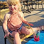 child, girl, blonde_hair, pink_top, wicker_chair, outdoor, sunny, drink, straw, blue_table, sandals, smiling, happy, summer, daylight, casual_clothing, portrait, face, legs, relaxing