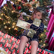 Addilynn joined the competition — help win amazing prizes! child, girl, christmas_tree, christmas_lights, ornaments, presents, gift_wrap, holiday, festive, sitting, indoors, living_room, candid, playful, bare_feet, pajamas, patterned_clothing, portrait, young_child, holiday_decorations