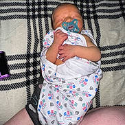 Asher joined the competition — help win amazing prizes! baby, newborn, infant, pacifier, swaddle, blanket, plaid_pattern, sleeping, hand, face, head, onesie, leg, adult_leg, smartphone, flash, indoors, close_up, skin, nursery