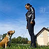 Ura a rejoint le concours — aidez-le/la à gagner de superbes lots ! dog, person, woman, outdoor, grass, daisies, sky, blue_sky, sunny, suburban, house, leash, collar, sitting, standing, pet, handler, black_jacket, black_pants, portrait
