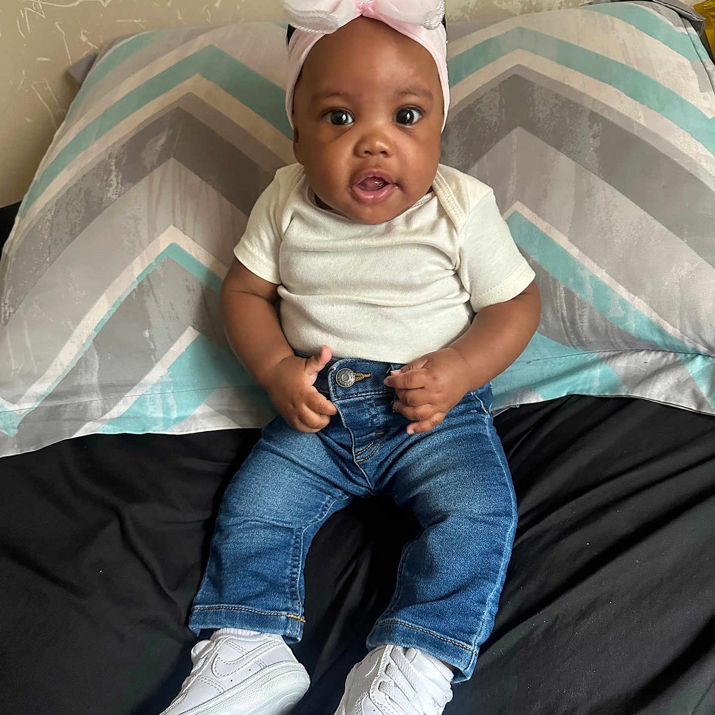 Trumoni joined the competition — help win amazing prizes! baby, child, headband, pink_bow, white_tshirt, blue_jeans, white_sneakers, bed, pillow, chevron_pattern, curious, sitting, indoors, person, cute, smiling, hands, young_child, portrait, casual_clothing