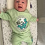 baby, infant, crib, green_clothing, smiling, face, cute, socks, stars_pattern, moon_pattern, sleeping_area, child, happy, soft_toys, pajamas, person, indoors, laying_down, comfort, cozy