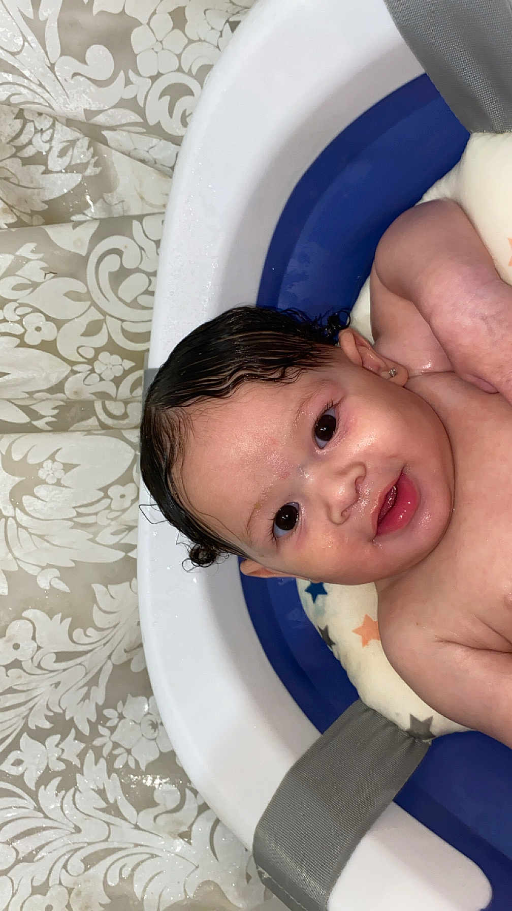 Delani is registered to the contest to win money with this photo: baby, bathtub, wet_hair, child, face, skin, earring, water, blue, white, curtain, pattern, smile, happy, infant, padded_tub, cute, indoors, portrait, young_child