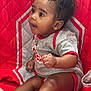 baby, child, infant, cute, sitting, red_quilt, gray_clothing, curly_hair, indoors, portrait, young_child, soft_lighting, happy, small_hands, barefoot, cozy, looking_away, cute_expression, fabric, quilting