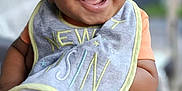 Marshall is registered to the contest to win money with this photo: baby, smiling, infant, bib, orange_clothing, happy, face, portrait, person, hand, holding, cute, child, skin, young, expression, outdoor, blurred_background, closeup, joyful