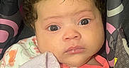Kehlani joined the competition — help win amazing prizes! baby, infant, child, portrait, face, eyes, curly_hair, looking_at_camera, serious, carrier, blanket, pacifier, clothing, pink, patterned, indoor, close_up, seated, soft_blanket, photography