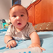 Adam is registered to the contest to win money with this photo: baby, infant, bed, bottle, wooden_headboard, pillow, blanket, room, diapers, window, curtains, clothing, hand, face, person, indoor, blue, brown, expression, child