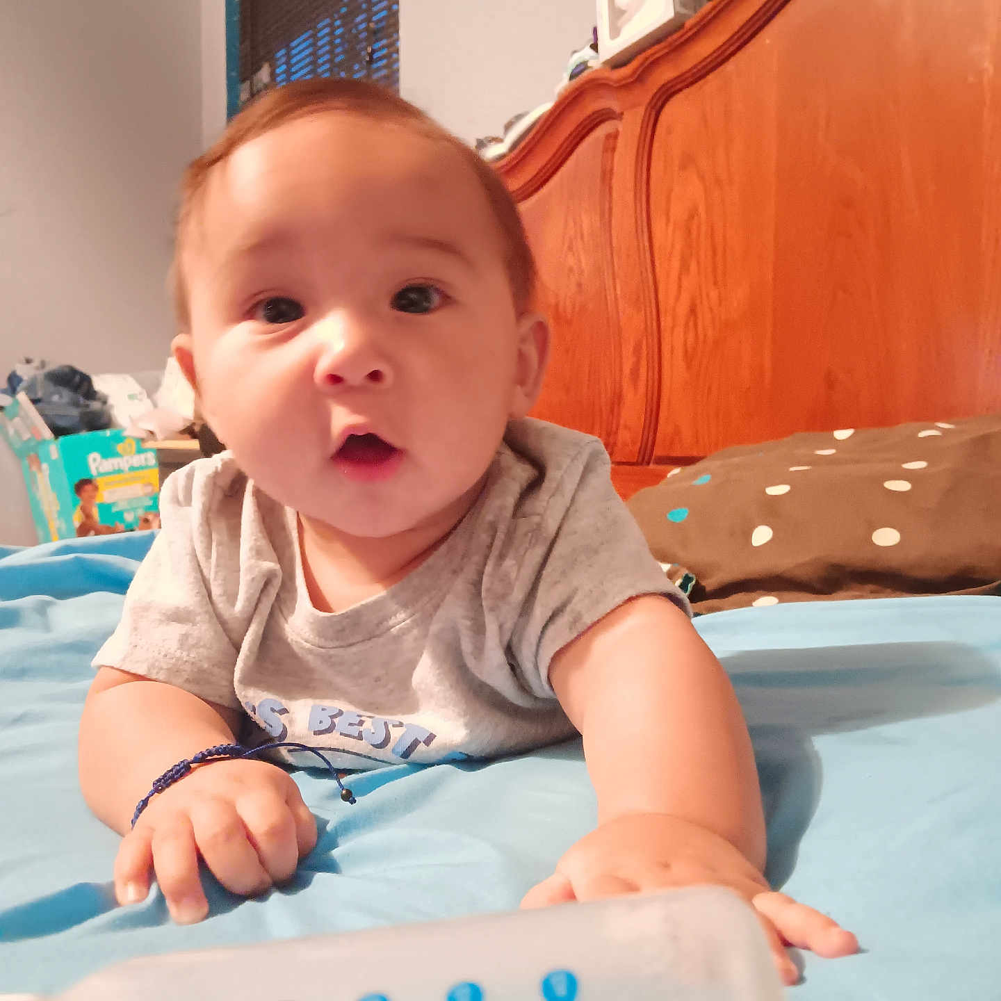 Adam is registered to the contest to win money with this photo: baby, bed, blanket, blue, bottle, brown, child, clothing, curtains, diapers, expression, face, hand, indoor, infant, person, pillow, room, window, wooden_headboard