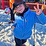 child, skiing, snow, helmet, blue_jacket, orange_helmet, peace_sign, winter, ski_poles, ski_boots, outdoor, snow_sports, safety_net, mountains, cold_weather, fun, playful, recreation, person, ski_goggles