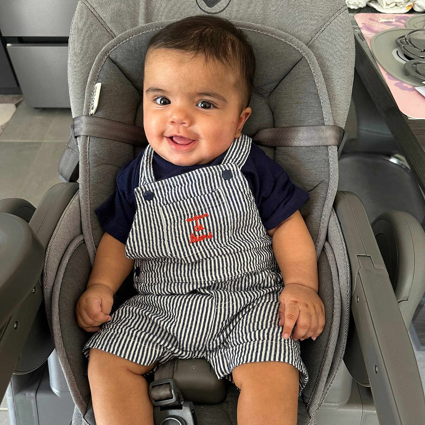 Maël a rejoint le concours — aidez-le/la à gagner de superbes lots ! baby, child, cloth, cushion, face, furniture, happy, high_chair, indoor, infant, kitchen, modern, navy_shirt, overalls, person, seat_belt, smiling, striped_clothing, table, wooden_legs