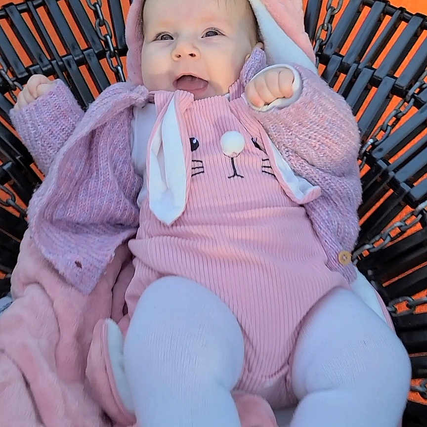 Kalinsa participe au concours pour gagner de l'argent avec cette photo : baby, infant, pink_clothing, bunny_ears, swing_chair, blanket, happy, smiling, outdoor, child, cute, portrait, warm_clothing, tights, cozy, person, seat, playful, young_child, fun