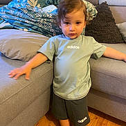Ahmed a rejoint le concours — aidez-le/la à gagner de superbes lots ! child, barefoot, adidas, tshirt, shorts, couch, pillow, living_room, floor, wooden_floor, person, indoor, furniture, young_child, standing, casual_clothing, home, relaxation, curly_hair, comfort