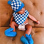 baby, infant, child, bib, checkered_pattern, blue_hat, blue_booties, diaper, couch, tufted_sofa, sitting, looking_sideways, plush_booties, soft_furniture, indoors, cute, adorable, portrait, hat_with_ears, studio_style
