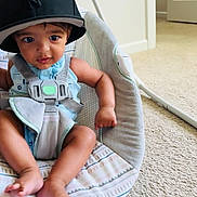 Kai Eli is registered to the contest to win money with this photo: baby, child, infant, hat, cap, baby_seat, car_seat, blue_clothing, straps, indoor, carpet, door, curious_expression, sitting, barefoot, person, young_child, cushion, home_interior, cute