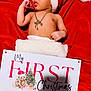 Kai Eli is registered to the contest to win money with this photo: baby, infant, christmas, santa_hat, red_background, holiday, first_christmas, sign, necklace, bracelet, bare_chest, blanket, portrait, lying_down, festive, teddy_bear_illustration, gifts, seasonal, cozy, celebration
