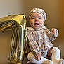 baby, child, plaid_clothing, hat, white_socks, balloon, number_one, celebration, smile, happy, portrait, sitting, cute, infant, first_birthday, indoors, baby_girl, clothing, face, headwear