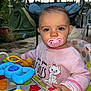 Leewene participe au concours pour gagner de l'argent avec cette photo : baby, pacifier, toy, activity_chair, outdoor, tent, sweater, child, face, hand, green, pink, blue, yellow, playtime, person, cute, expression, nature, seat