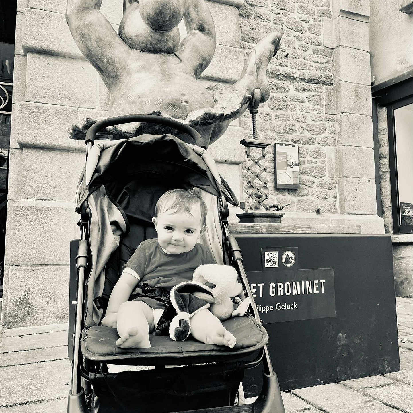 Leewene a rejoint le concours — aidez-le/la à gagner de superbes lots ! baby, black_and_white, building, child, happy, infant, outdoor, person, portrait, public_space, seat, sidewalk, smiling, statue, stone_wall, stroller, stuffed_toy, toy, urban, window
