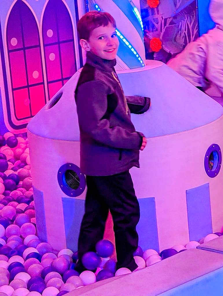 Giovanni is registered to the contest to win money with this photo: child, boy, smiling, ball_pit, play_area, indoor, colorful, purple, pink, jacket, pants, toy, play_structure, fun, leisure, recreation, happy, person, lighting, entertainment