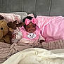 baby, child, pink_bow, bib, cartoon_cat, plush_toy, moose, blanket, pillow, bed, headboard, smile, indoor, cozy, soft_texture, happy, clothing, infant, person, portrait