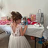 Yrina a rejoint le concours — aidez-le/la à gagner de superbes lots ! child, girl, white_dress, lace, plush_toy, gift_bags, table, party, celebration, decorations, balloon, indoors, floor, hair_updo, back_view, present, pink, white, person, tulle