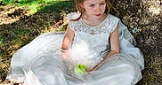 Yrina a rejoint le concours — aidez-le/la à gagner de superbes lots ! child, girl, white_dress, apple, tree, grass, outdoor, nature, sitting, sunlight, shadows, sandals, young, portrait, casual, daylight, leafy, ground, thoughtful, calm