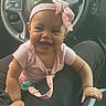 baby, child, smiling, headband, pink, bow, car_interior, steering_wheel, person, seat, clothing, happy, infant, sitting, lap, cute, young, portrait, close_up, hands