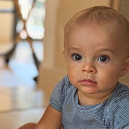 Lelio participe au concours pour gagner de l'argent avec cette photo : baby, child, infant, face, eyes, striped_clothing, onesie, sitting, floor, indoor, portrait, cute, curious, skin, head, person, young, expression, closeup, blurred_background
