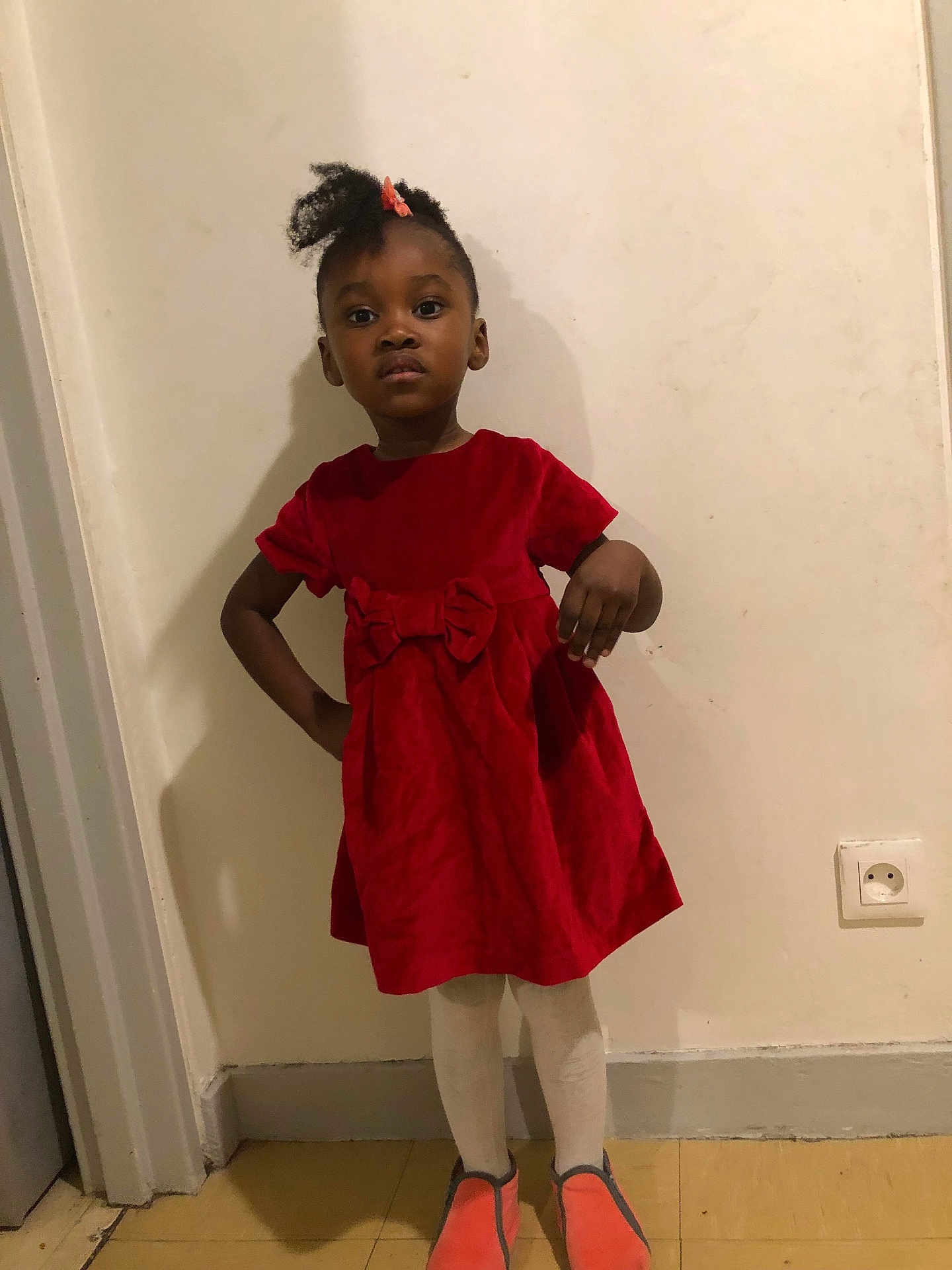 Alyssa participe au concours pour gagner de l'argent avec cette photo : bow, casual, child, confident, expression, floor, girl, hair_clip, indoor, orange_slippers, person, portrait, posing, power_outlet, red_dress, shadow, standing, tights, wall, young