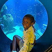 Alyssa a rejoint le concours — aidez-le/la à gagner de superbes lots ! aquarium, blue_background, braids, casual_clothing, child, cute, denim_shorts, fish, girl, happy, indoor, leisure, marine_life, portrait, rocks, sitting, smiling, underwater, white_shoes, window