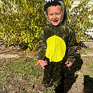 Legend Fox is registered to the contest to win money with this photo: bushes, child, costume, daylight, dinosaur_costume, footwear, grass, green, happy, hood, house, nature, outdoor, person, playful, portrait, smiling, sunlight, wall, yellow