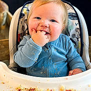 Parker joined the competition — help win amazing prizes! baby, child, high_chair, messy, crumbs, blue_onesie, snack_time, face, hand, smile, happy, indoor, person, cute, infant, food, table, seat, blond_hair, cheeks