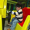 Thiago G joined the competition — help win amazing prizes! child, toddler, boy, indoor, playground, amusement_park, ride, race_car, steering_wheel, sitting, profile, focused, striped_shirt, jeans, shoes, colorful, yellow, red, play_structure, portrait