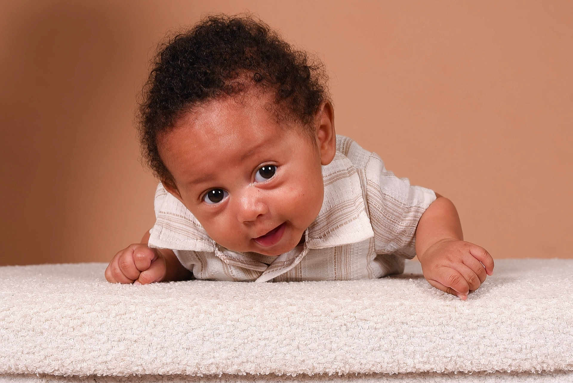 Ismaël a rejoint le concours — aidez-le/la à gagner de superbes lots ! baby, infant, child, curly_hair, smiling, lying_down, white_clothing, soft_texture, close_up, portrait, cute, playful, looking_at_camera, indoor, skin, face, head, hand, expression, background