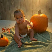 Jayden is registered to the contest to win money with this photo: baby, diaper, pumpkin, green_blanket, wooden_wall, autumn, child, indoor, soft_light, curious, sitting, orange, cute, toddler, floor, skin, portrait, seasonal, warm_light, cozy