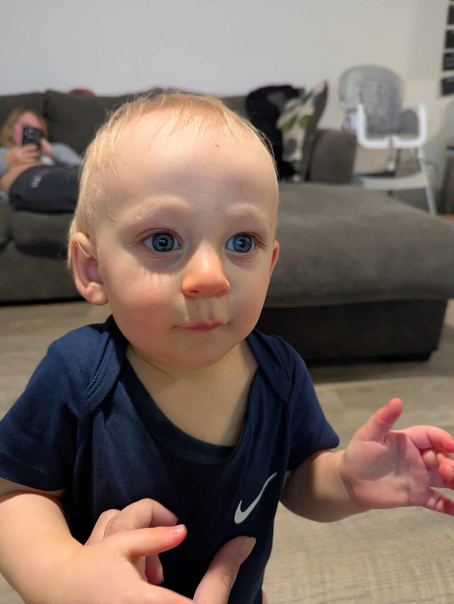 Hudson joined the competition — help win amazing prizes! toddler, child, blue_eyes, navy_shirt, hand, living_room, couch, woman, phone, high_chair, floor, person, indoors, curious_expression, baby, short_hair, skin, holding, background, casual