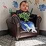 child, toddler, small_chair, armchair, leather_chair, nursery_wall, animal_wall_stickers, elephant_sticker, monkey_sticker, flamingo_sticker, carpet, socks, sweatshirt, blue_pants, sitting, portrait, sunlight, shadow, curious_expression, indoor