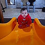 child, baby, toddler, orange_slide, red_hoodie, crawling, hands, face, expression, indoor_playarea, tiles, chairs, table, window, reflection, backpack, playground_equipment, portrait, floor, restaurant_interior