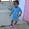 Keith is registered to the contest to win money with this photo: child, boy, outdoor, sidewalk, mickey_mouse, blue_clothing, shorts, sneakers, holding_object, curious_expression, pink_wall, door, concrete, hair_braids, casual_wear, street, urban, person, daylight, standing