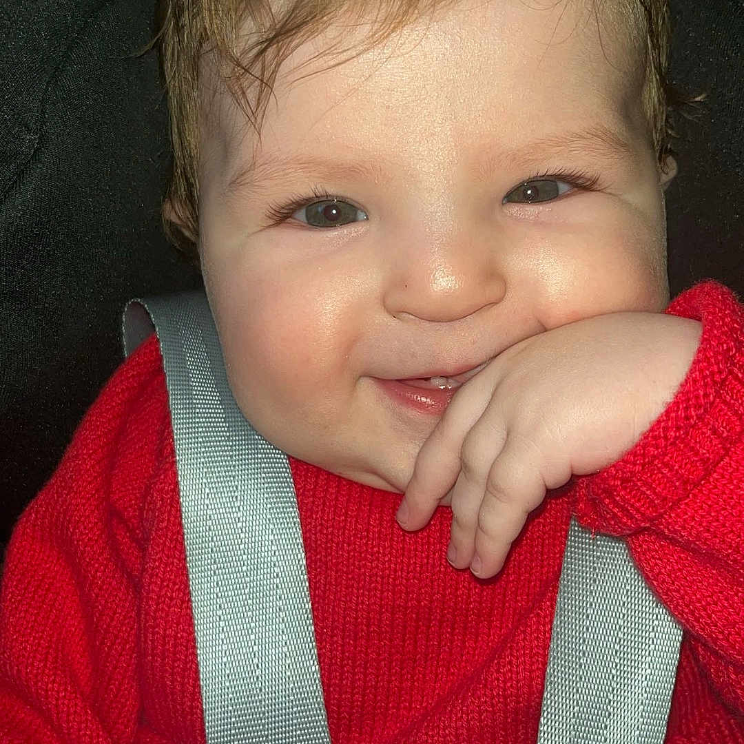 Lehna Jasmine a rejoint le concours — aidez-le/la à gagner de superbes lots ! baby, car_seat, cheeks, child, closeup, clothing, cute, face, hair, hand, happy, harness, indoor, infant, person, portrait, red_sweater, seatbelt, skin, smile